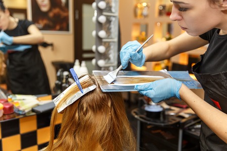 Professional hairdresser dyeing hair of her client in salon. Selective focus.の写真素材