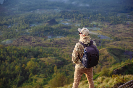 Man tourist looks at the sunrise on the volcano Batur on the island of Blai in Indonesia. Hiker man with backpack travel on top mountain, travel conceptの写真素材