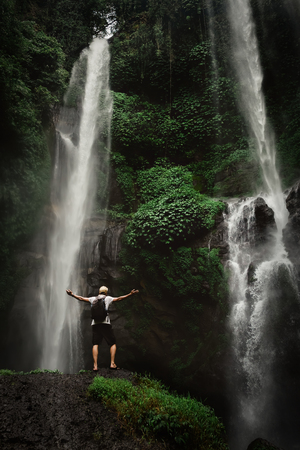 Man enjoying waterfall raised hands. Travel Lifestyle and success concept vacations into the wild nature on background mountain and rainforest.の写真素材