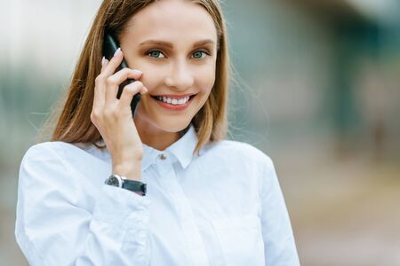 Young famale calling on a smartphone. Attractive businesswoman talking by phone. Office building...