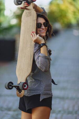 Beautiful young woman with longboard on the city street in sunny weather. Young hipster girl posing with longboard, skateboard, streetphoto, life style, freedom, happy face.の写真素材