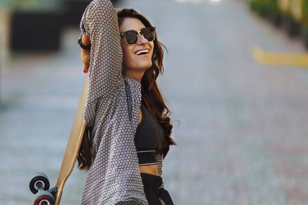 Beautiful young woman with longboard on the city street in sunny weather. Young hipster girl posing with longboard, skateboard, streetphoto, life style, freedom, happy face.の写真素材