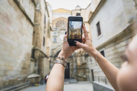 Girl makes a photo or video on the phone. Hands hold a smartphone and make a photo with landmark in the europe old townの写真素材