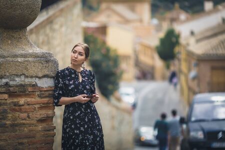 Pretty young woman in a black dress using smartphone at old town street. Travel by Europe. Toledo, Spainの写真素材