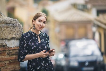 Pretty young woman in a black dress using smartphone at old town street. Travel by Europe.の写真素材