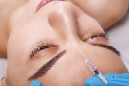 Closeup Portrait of young Caucasian woman getting cosmetic injection in forehead. People, cosmetology, plastic surgery and beauty concept.の写真素材