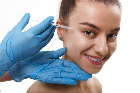 Facial Beauty Injections. Portrait Beautiful Young Woman Receiving Hyaluronic Acid Injection. Closeup Of Hands In Gloves Holding Syringe Near Attractive smiling Female Face.の写真素材