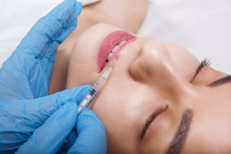 Facial Beauty Injections. Portrait Beautiful Young Woman Receiving Hyaluronic Acid Injection. Closeup Of Hands In Gloves Holding Syringe Near Attractive Female Face.の写真素材