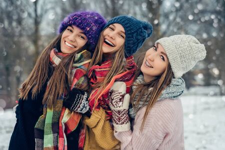 Three women friends outdoors in knitted hats having fun on a snowy cold weather. Group of young female friends outdoors in winter park.の写真素材
