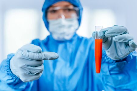 Medic in hazmat protective suit holds a test tube with a coronavirus positive blood sample . 2019 nCoV pandemic. stop coronavirus. MERS.の写真素材