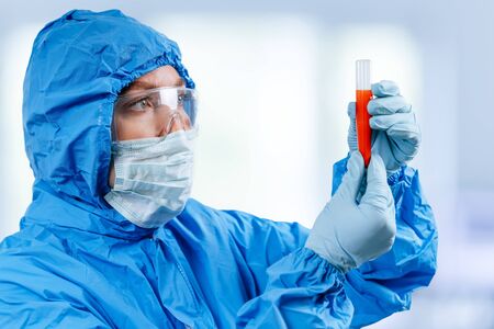 Medic in hazmat protective suit holds a test tube with a coronavirus positive blood sample. 2019 nCoV pandemic. stop coronavirus. MERS.の写真素材