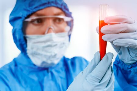 Medic in hazmat protective suit holds a test tube with a coronavirus positive blood sample. 2019 nCoV pandemic. stop coronavirus. MERS.の写真素材