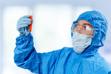 Medic in hazmat protective suit holds a test tube with a coronavirus positive blood sample. 2019 nCoV pandemic. stop coronavirus. MERS.の写真素材