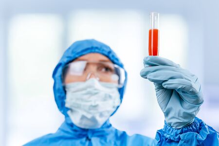 Medic in hazmat protective suit holds a test tube with a coronavirus positive blood sample. 2019 nCoV pandemic. stop coronavirus. MERS.の写真素材