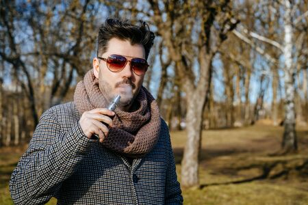 Confident young bearded male in sunglasses vape electronic cigarette. A young handsome bearded...