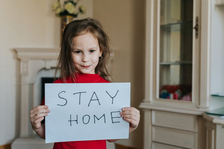 Stay at home concept. Small girl in red T-shirt holding sign saying stay at home for virus protection. Quarantine concept.の写真素材