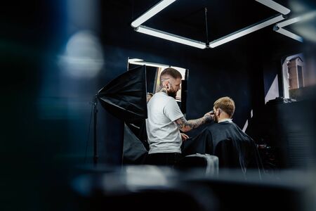 Male haircut with electric razor. Tattooed Barber makes haircut for client at the barber shop by using hairclipper. Man hairdressing with electric shaver.の写真素材