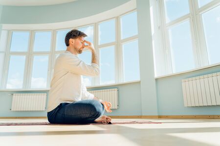 Man practice yoga. Young attractive male doing breathing exercises. Guy meditating at home along during the pandemic. Relaxation and resting concept for isolation. Slide shot.の写真素材