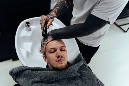 Attractive male is getting a modern haircut in barber shop. Top view of a young man getting his hair washed and his head massaged in a hair salonの写真素材