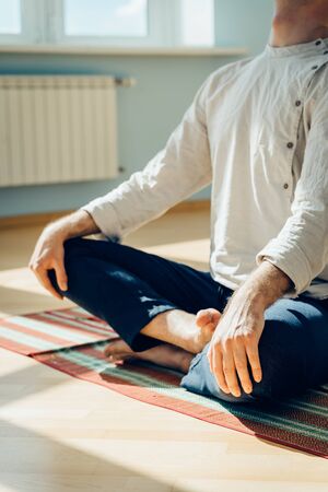 Man practice yoga. Young attractive male doing breathing exercises. Guy meditating at home along during the pandemic. Relaxation and resting concept for isolation. Slide shot.の写真素材