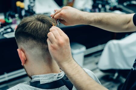Tattooed Barber cuts the hair of the client with scissors. Close up. Attractive male is getting a modern haircut in barber shop. Close up view.の写真素材