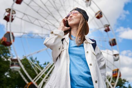 Summer lifestyle portrait woman enjoy nice day, talking smartphone. Happy female in front of ferris wheel. Young girl having fun, joy.の写真素材