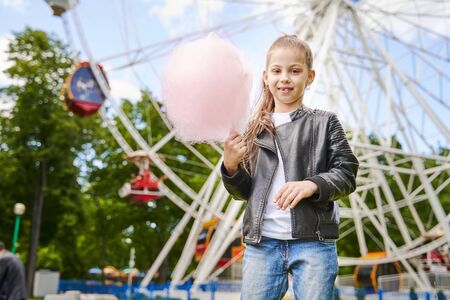 Portrait of a child with sweet cotton candy. A little girl on the background of ferris wheel is eating candy-floss summer sunny day.の写真素材