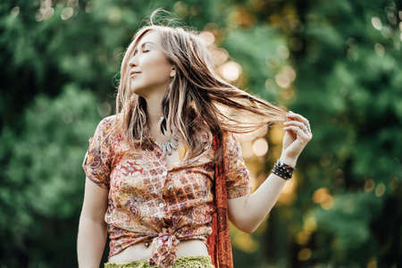 Beautiful young woman wearing bohostyle clothes posing in the rays of the evening sun, sunset. Boho...