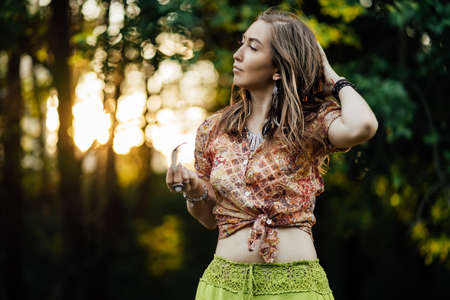 Portrait of Beautiful young woman wearing bohostyle clothes posing in the rays of the evening sun, sunset. Boho style fashion, female wearing silver jewelry having fun in park outdoors.の写真素材