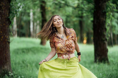 Portrait of Beautiful young woman wearing bohostyle clothes posing in the rays of the evening sun, sunset. Boho style fashion, female wearing silver jewelry having fun in park outdoors.の写真素材