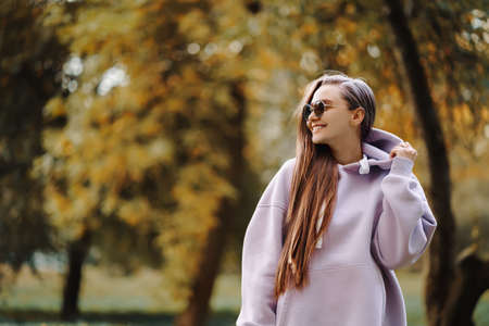 Beautiful happy smiling young woman wearing pink hoodie walking in autumn park. Season and people concept.の写真素材