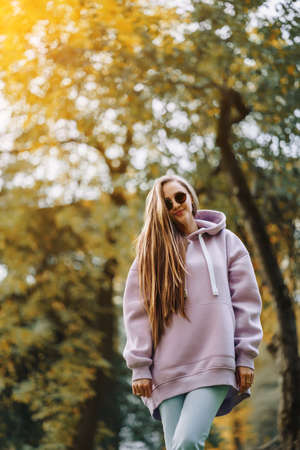 Beautiful happy smiling young woman wearing pink hoodie walking in autumn park. Season and people concept.の写真素材