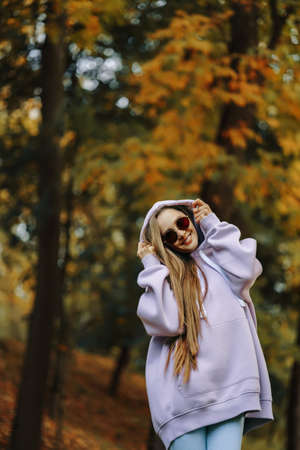 Young woman wearing pink hoodie and jeaans in the park at sunny autumn day. Season and people concept.の写真素材