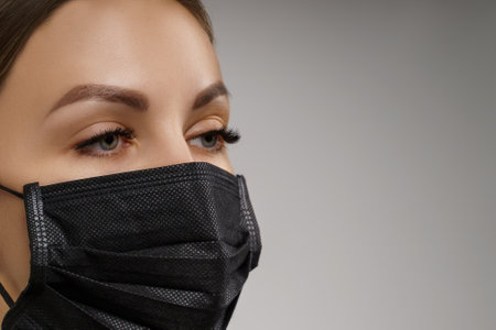 Eyelash Extension Procedure. Beautiful Woman with Extreme Long False Eyelashes. Makeup, Cosmetics. Beauty, Skincare. Woman in medical mask.の写真素材