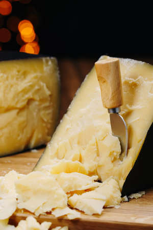 Medium hard cheese head parmesan on wooden board, with cheese parmesan knifes.