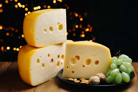 Cheese on table with grapes and nuts. Medium hard cheese head edam, gouda, parmesan on wooden board. Healthy eating concept.の写真素材