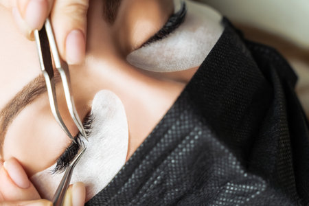 Eyelash Extension Procedure. Beautiful Woman with Extreme Long False Eyelashes. Makeup, Cosmetics. Beauty, Skincare. Woman in medical mask.の写真素材