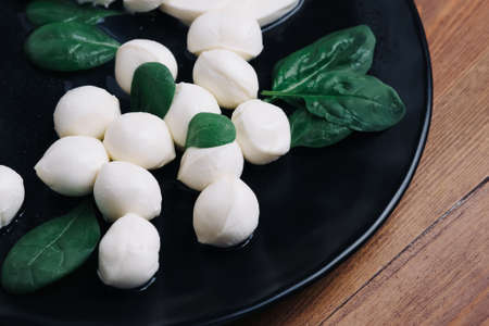 White small mozzarella cheese balls, spinach leaves and tomatoes on black plate.の写真素材