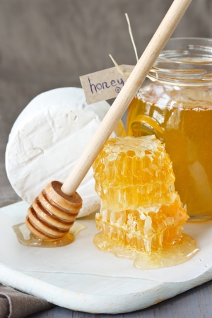 Jar of honey, delicious honeycombs and camembert on a wooden board.の写真素材