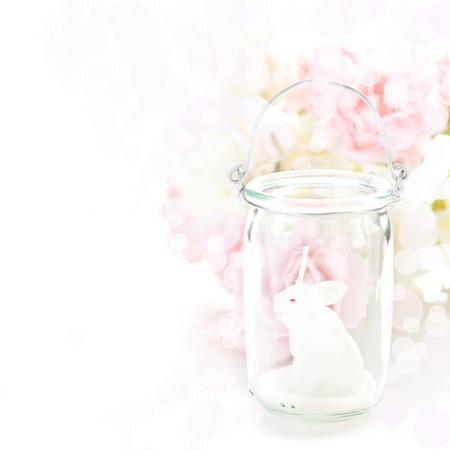 Easter white bunny candle in a glass jar with soft roses and bokeh.の写真素材