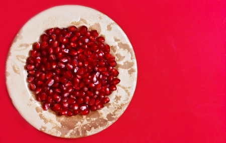 Sweet ripe pomegranate seeds in a rustic plate on a red background の写真素材