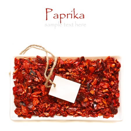 Flakes of dry paprika in a bowl with empty tag on a white background の写真素材