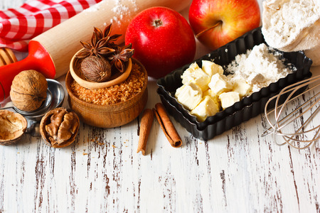 Ingredients for apple pie cooking. Fresh red apple, butter, flour, brown sugar, nuts and spices on a rustic wooden background.の写真素材