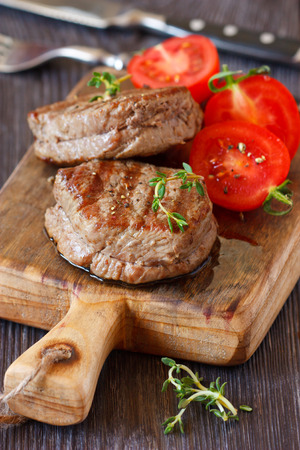 Juicy beef steak with tomato salad served on an old wooden cutting board.の写真素材