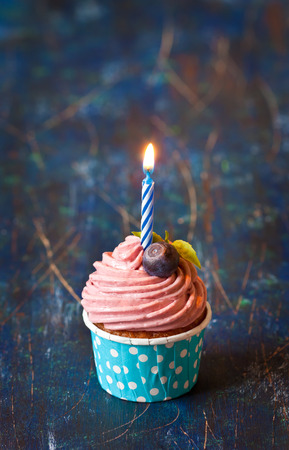 Delicious blueberry cupcake with birthday candle on an old wooden board.の写真素材