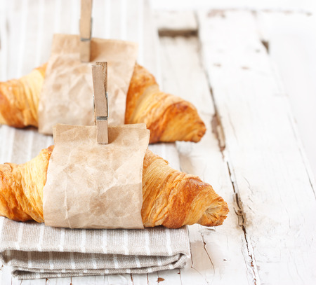 Fresh croissants wrapped in paper on an old white board.の写真素材