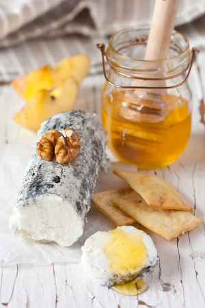 Delicious goat cheese with honey, walnuts and crackers on an old wooden cooking board.の写真素材