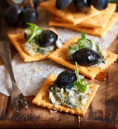 Delicious blue cheese crackers appetizer with honey, grape and arugula on an old cooking board.の写真素材