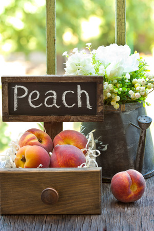 Sweet summer peaches in rustic wooden box and white flowers in the watering can on a garden.の写真素材