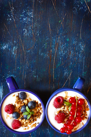 Yogurt with granola and fresh berries on an old wooden board.の写真素材